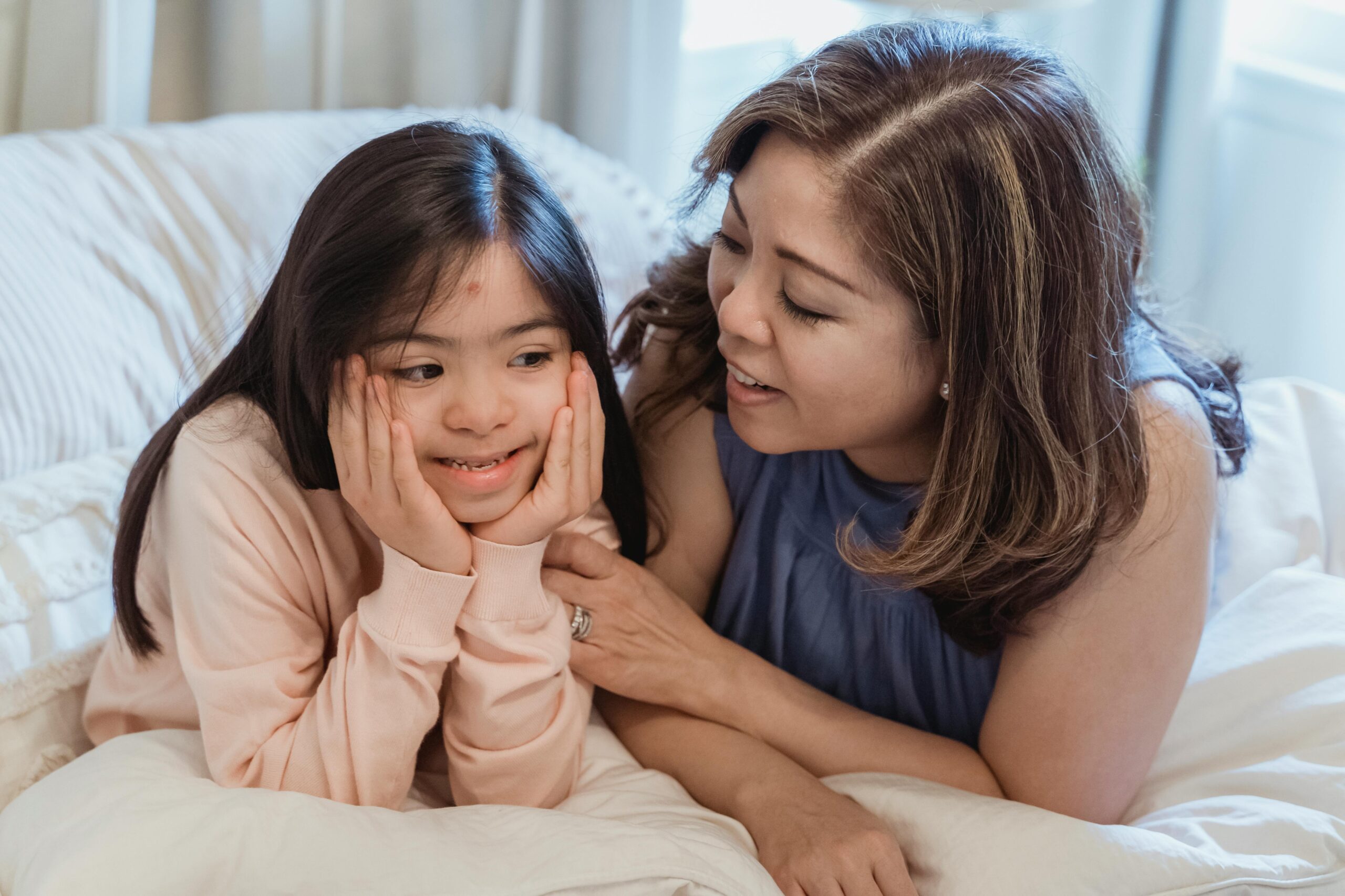 Tender moment between a mother and her daughter with Down syndrome, smiling in bed.